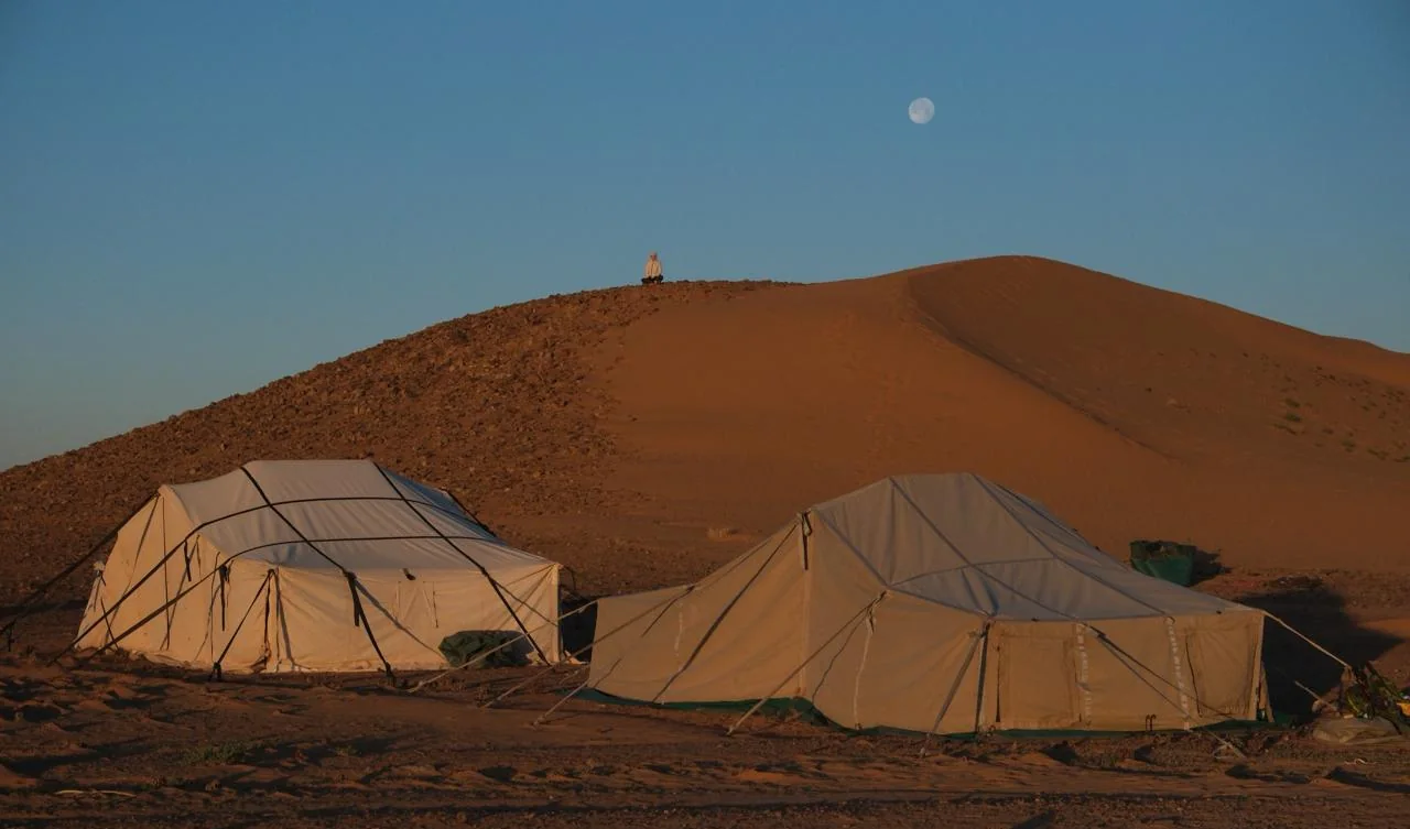 Two canvas bivouac tents beneath the moon in the Moroccan desert